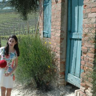 la giovane attrice Alice Borghetto tiene in mano il gomitolo di lana rossa che lanciato tra i filari scandisce il racconto delle tradizioni, di generazione in generazione