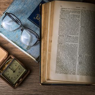 pagine di un libro aperto accanto a un paio di occhiali e un orologio