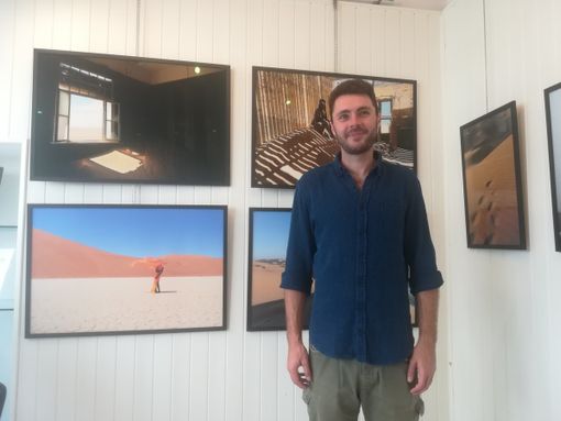 Il fotografo Gregory Pepper ritratto con alle spalle alcuni suoi scatti