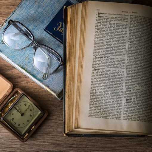 pagine di un libro aperto accanto a un paio di occhiali e un orologio