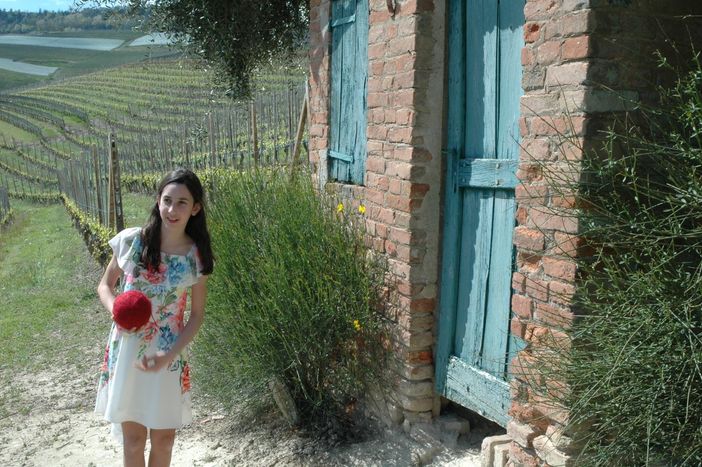 la giovane attrice Alice Borghetto tiene in mano il gomitolo di lana rossa che lanciato tra i filari scandisce il racconto delle tradizioni, di generazione in generazione