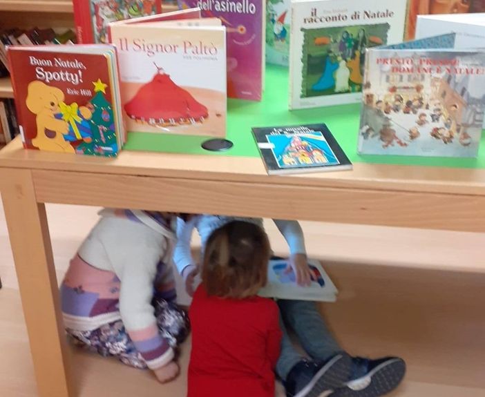 Alcuni bambini giocano sotto un tavolo della Biblioteca Monticone di Canelli